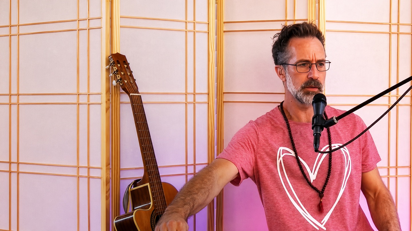 Alex King-Harris leading a live breathwork, voice and music session — at the mic with a guitar beside him